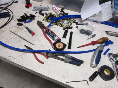 Workbench with tools and automotive parts, including pliers, screwdrivers, spark plugs, and blue wire.