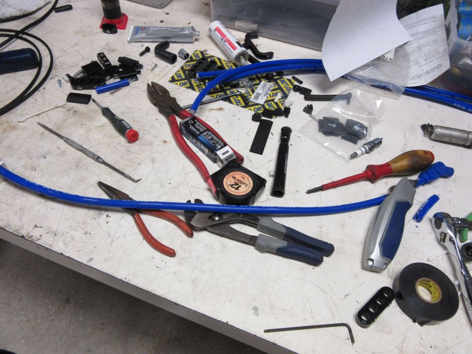 Workbench with tools and automotive parts, including pliers, screwdrivers, spark plugs, and blue wire.