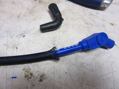 Damaged black braided wire loom with blue spark plug wire and black rubber boot.