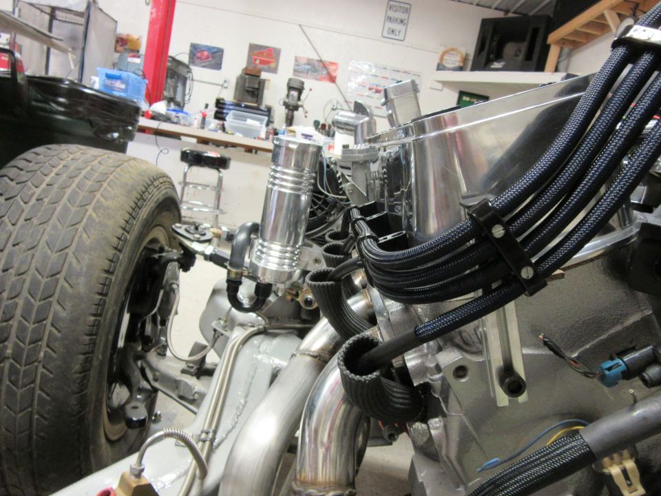 Close-up of engine bay with aluminum intake, braided hoses, and tire.