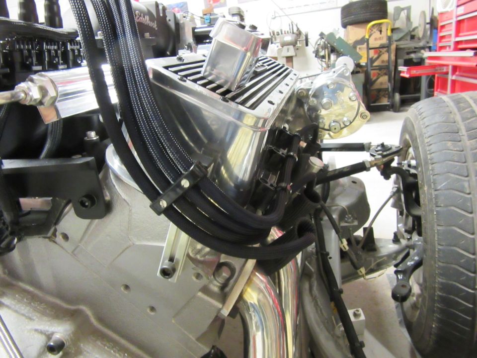 Polished aluminum engine with chrome valve cover and black fuel lines, tire and suspension visible.