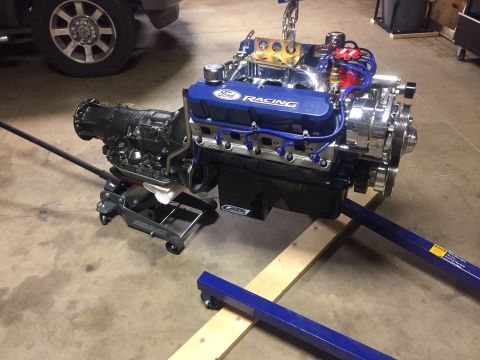 1982 Ford Bronco - A Ford V8 engine and automatic transmission assembly, painted blue and chrome, is supported by an engine hoist and a floor jack in a garage…