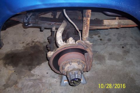 1973 Ford F-250 - The rear suspension and brake assembly of a blue pickup truck is shown, supported by a jack stand. The image captures the leaf springs, sho…