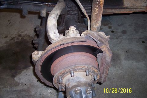 1973 Ford F-250 - A close-up view of the front brake assembly of a vehicle, showing a rusty brake rotor, caliper, and suspension components. The image is dat…