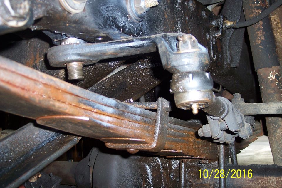 Close-up of truck steering linkage and rusty leaf springs.