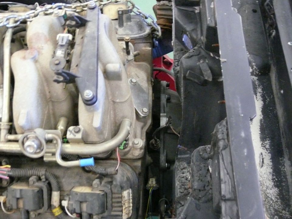 Vehicle engine bay with intake manifold and damaged, charred frame section.