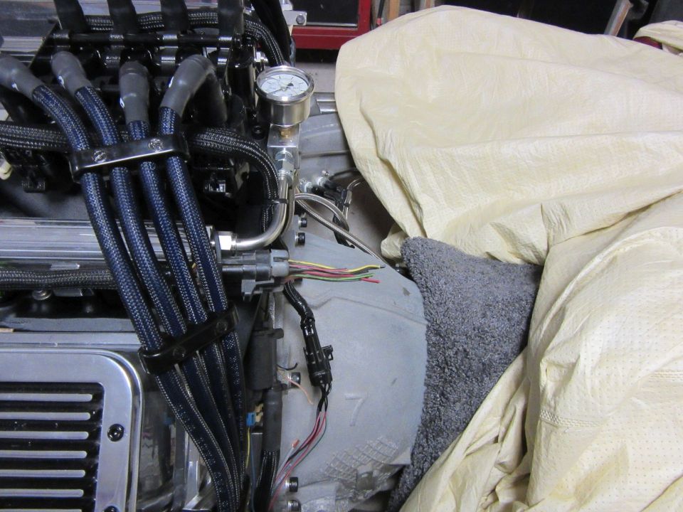 Vehicle engine bay with spark plug wires, pressure gauge, and tarp.