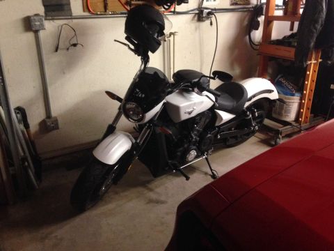 2010 Dodge Challenger - A white and black motorcycle is parked in a garage next to a red car. A black helmet is mounted on the handlebars of the motorcycle.