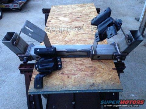 1971 Ford Ranchero - A custom fabricated metal subframe assembly with two black engine mounts is shown mounted on a piece of plywood.