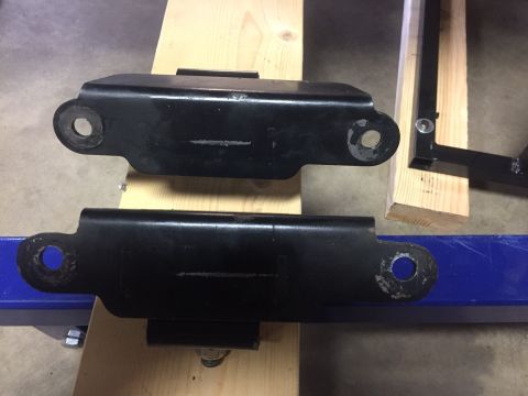 1982 Ford Bronco - Two black metal brackets with circular mounting holes are shown. The brackets are resting on wooden planks, with one bracket positioned abo…
