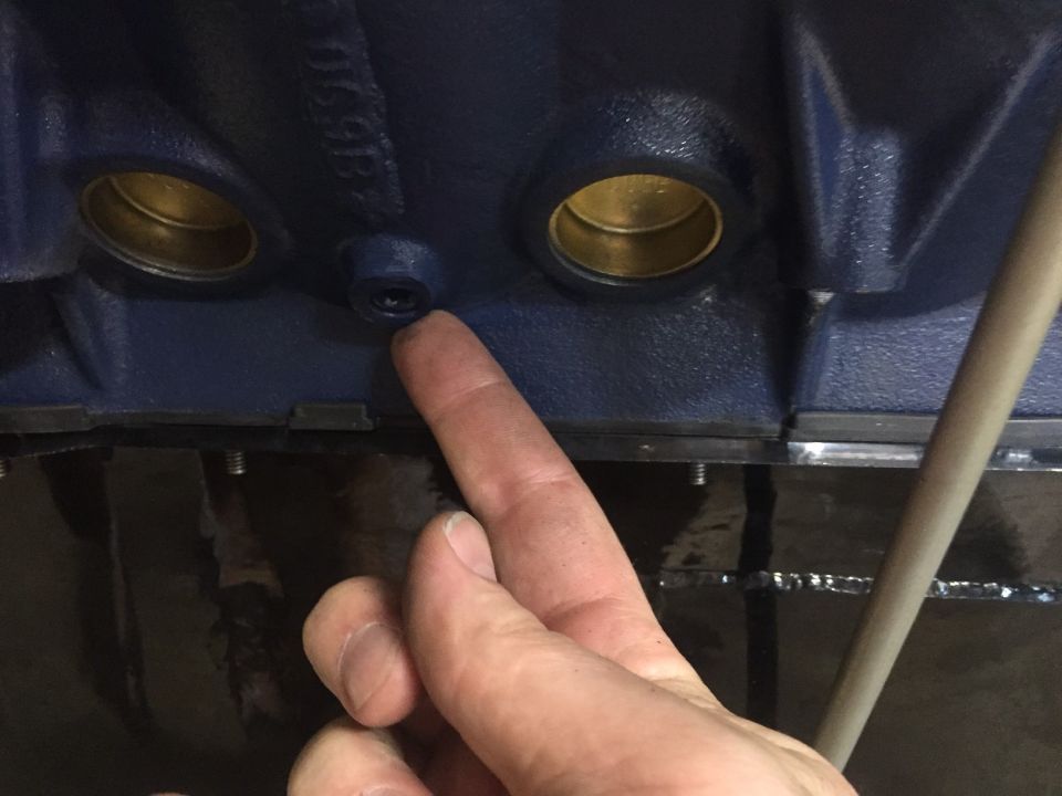 Close-up of a dark blue engine block with a finger pointing to a small hole.