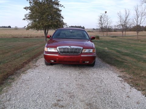 1999 Mercury Grand Marquis - The front view of a red Mercury Grand Marquis is parked on a gravel driveway with a field and trees in the background.