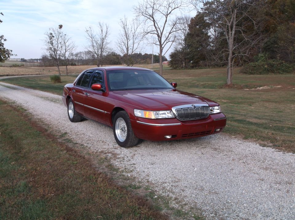 Red 1999 Mercury Grand Marquis sedan parked on a gravel driveway.