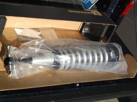 2005 Ford F-150 - A new FOX brand front shock absorber with a silver coilover spring is shown inside its opened cardboard box, placed in the bed of a dark-co…