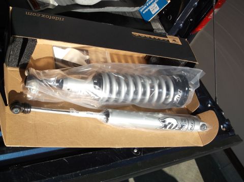 2005 Ford F-150 - A pair of new Fox 2.0 shocks with silver bodies and black springs are packaged in a cardboard box. The shocks are inside plastic wrapping,…
