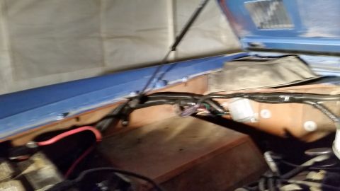 1973 Ford Bronco - Looking under an open hood with a blue underside, showing a tangle of wiring, hoses, and fuel components during a restoration.