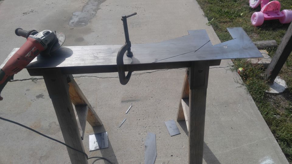 Angle grinder on sawhorse with metal sheet clamped for cutting. Pink toy wagon in background