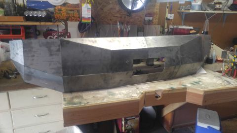 1991 Ford Bronco - Unfinished custom metal bumper with angular design and rectangular cutouts, resting on a workbench.