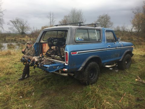 1979 Ford Bronco - A hunter sits in the back of a blue SUV, showing off a successful duck hunt.