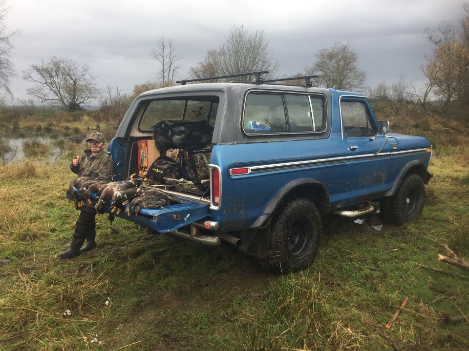 Blue SUV with tailgate down, showing hunting gear and ducks. A person gives a thumbs up