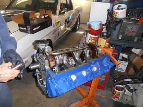 1972 Ford Bronco - A blue engine block is on an orange stand, with a person working on it and a white car in the background.