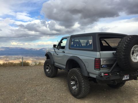 1988 Ford Bronco - This Ford Bronco is parked on a scenic overlook with mountains in the distance under a cloudy sky.