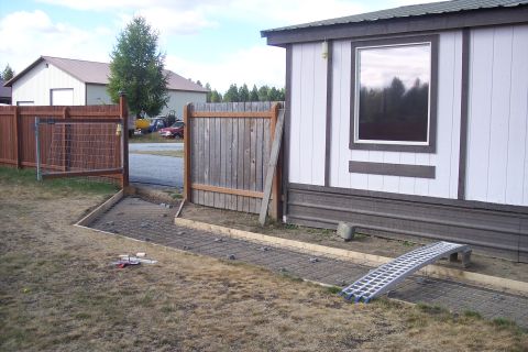 1989 Ford Bronco - A red SUV and a yellow truck are visible in the background, parked on gravel near a fence and a mobile home.