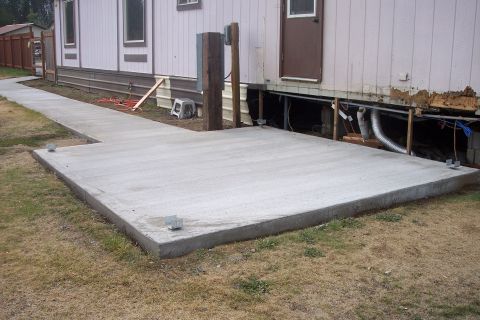 1989 Ford Bronco - A newly poured concrete patio and walkway are visible next to a mobile home with exposed foundation and utility lines.
