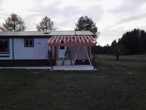 1989 Ford Bronco - A partially constructed wooden roof structure is being built over a concrete patio attached to a mobile home. Construction ladders are visi…