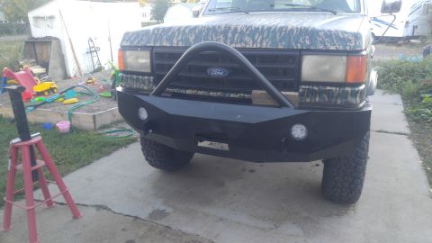 1991 Ford Bronco - Front view of a Ford Bronco with a custom black bumper and camouflage paint on the hood and grille. The vehicle is parked on a concrete dri…