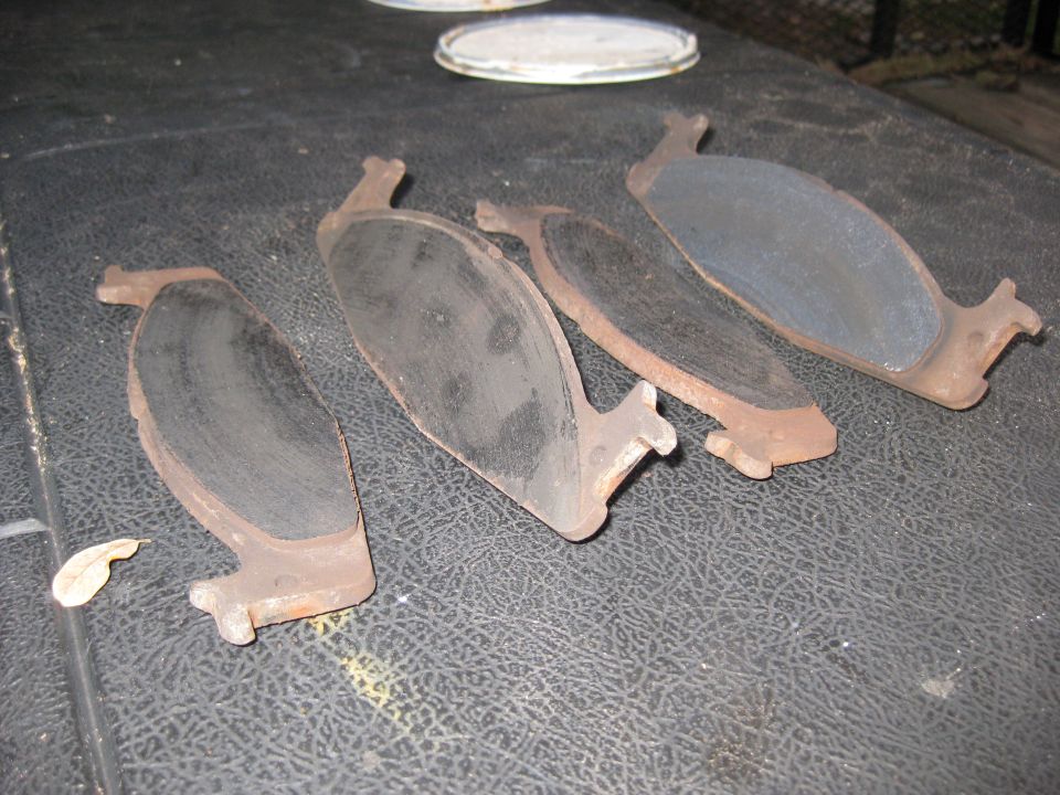 Four used brake pads on a black textured surface
