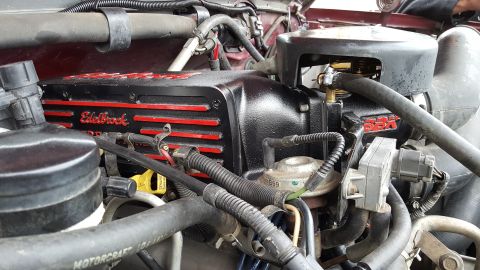 1996 Ford Bronco - Close-up view of the engine bay of a 1996 Ford Bronco, focusing on a black Edelbrock valve cover with red accents and a black air intake sy…