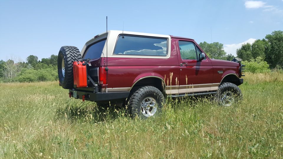 1996 Ford Bronco in a field with spare tire and jerrycan on rear bumper.