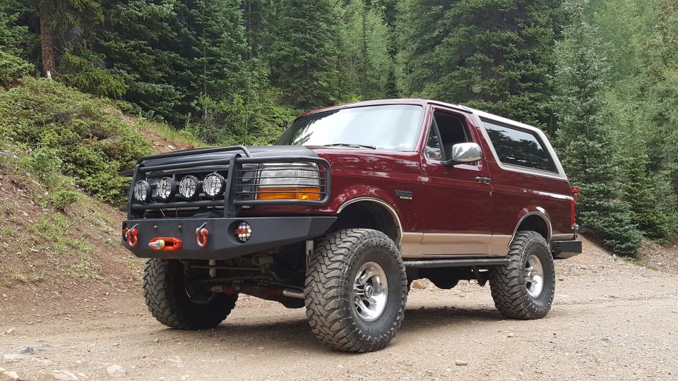 Lifted maroon 1996 Ford Bronco with custom bumper and brush guard in a forest.