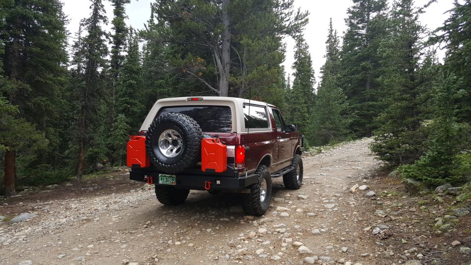 1996 Ford Bronco parked on a forest road with a spare tire and jerry cans on the back.