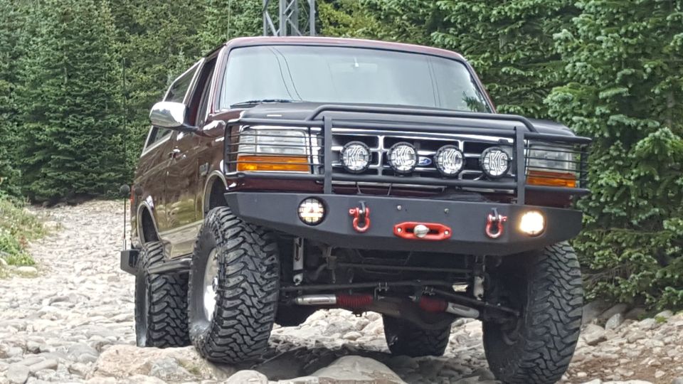 Lifted 1996 Ford Bronco with aftermarket bumper and KC lights on a rocky trail.