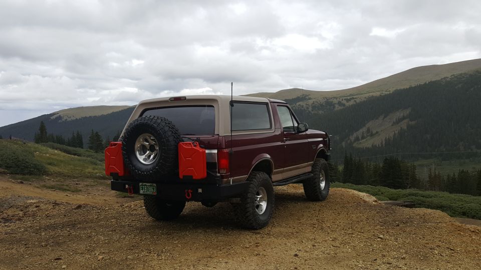 1996 Ford Bronco with spare tire and jerry cans parked on a mountain road.
