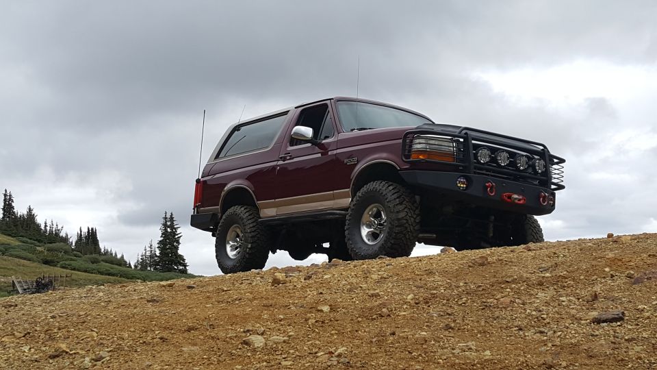 Maroon 1996 Ford Bronco with off-road mods on a dirt hill.