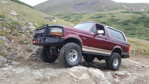 1996 Ford Bronco - A maroon 1996 Ford Bronco with a lifted suspension and off-road tires navigates a rocky mountain trail.