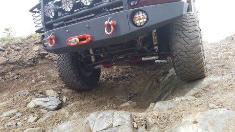 1996 Ford Bronco - A low-angle shot of the front bumper and tires of a modified off-road vehicle navigating rocky terrain. The vehicle features large, aggress…