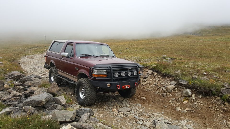 Maroon 1990s Ford Bronco on a rocky mountain trail in fog.