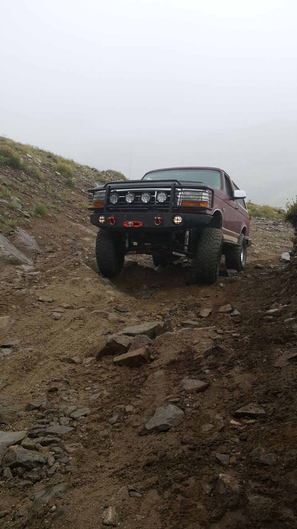 Maroon 1996 Ford Bronco on a rocky off-road trail with a winch and auxiliary lights.