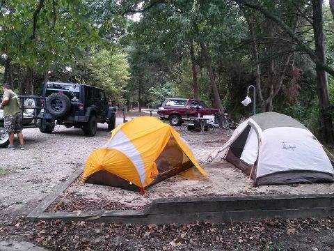 1996 Ford Bronco - Two tents are set up at a campsite next to a black Jeep Wrangler with a spare tire mounted on the back. A red Ford Bronco is parked in the…