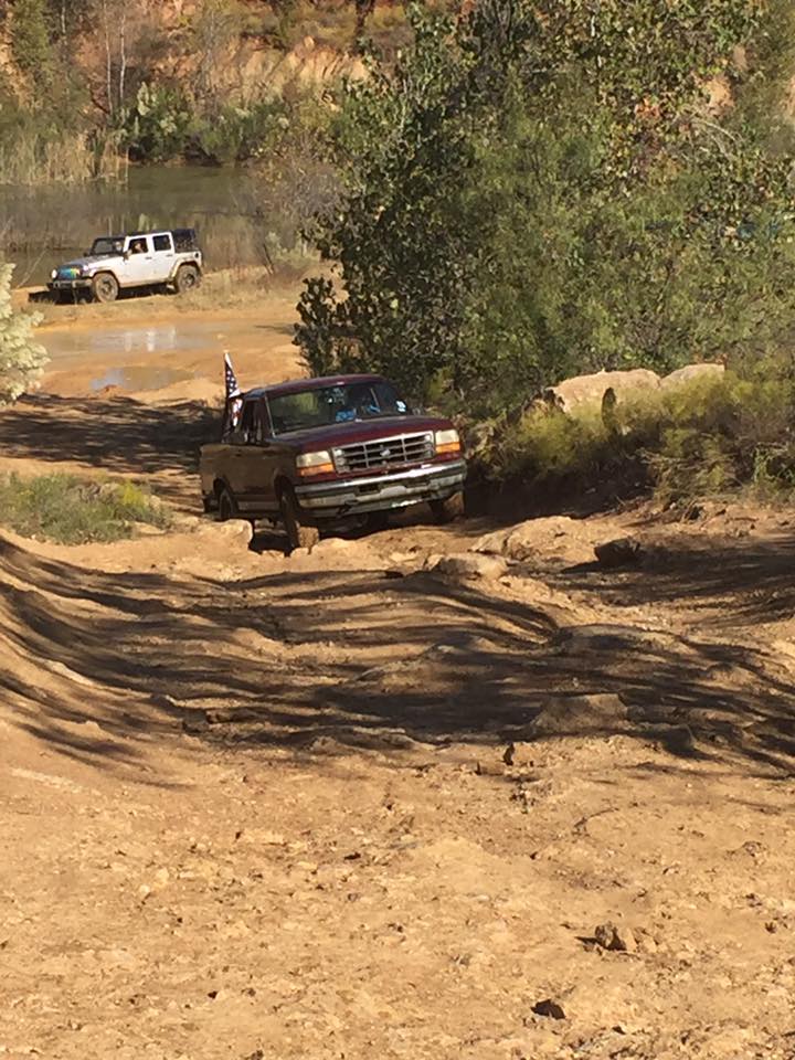 Maroon Ford pickup truck off-roading on a dirt path with a white Jeep in the background.