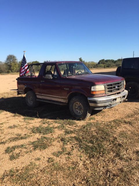 1996 Ford Bronco - A maroon 1996 Ford Bronco is parked in a dry, grassy field under a clear blue sky. An American flag is mounted on a roll bar behind the dri…