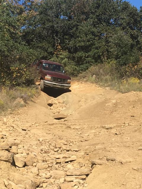 1996 Ford Bronco - A maroon 1990s Ford Bronco is navigating a challenging dirt trail with steep inclines and rocky terrain.