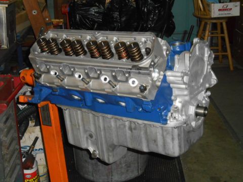 1972 Ford Bronco - A close-up view of a partially assembled V8 engine, painted blue and silver, mounted on an orange engine stand. The engine features exposed…