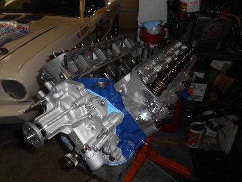 1972 Ford Bronco - A partially assembled V8 engine with a blue oil pan and silver aluminum heads is displayed on an engine stand in front of a classic white v…
