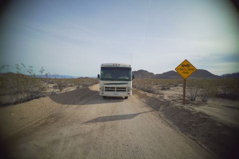 1995 Chevrolet P30 1 Ton - Step Van - Large Class A motorhome parked on a sandy desert trail beside a yellow 4 Wheel Drive Road warning sign.