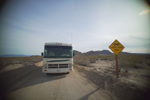 1995 Chevrolet P30 1 Ton - Step Van - A white and green RV is parked on a dirt road in a desert landscape. A yellow diamond-shaped sign warning of a "4 WHEEL DRIVE ROAD" is visi…